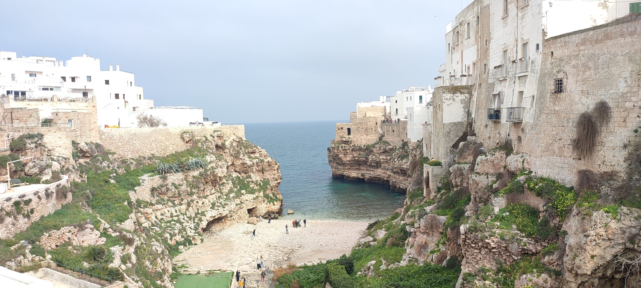 Veduta panoramica di Lama Monachile a Polignano a Mare con la spiaggia tra le scogliere, case bianche a picco sul mare e il mare cristallino.